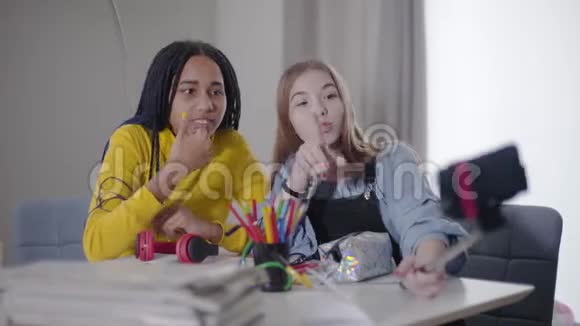 两个朋友一起制作视频博客的肖像白人和非裔美国少女看智能手机视频的预览图