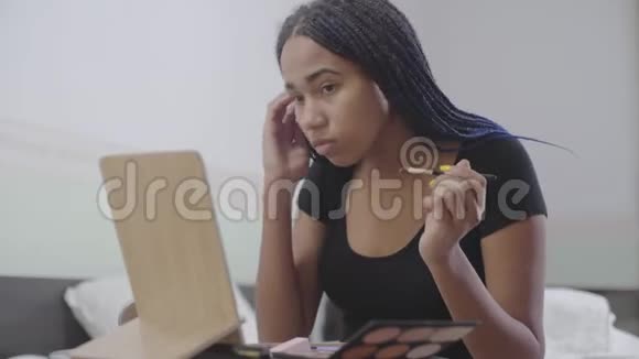 可爱的非裔美国女孩在右眼上涂上眼影带着恐惧的少年看着镜子做着视频的预览图