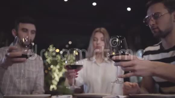 两个男人和女人坐在现代土耳其餐馆的桌子旁用红酒叮叮当当地眨着眼睛朋友们视频的预览图