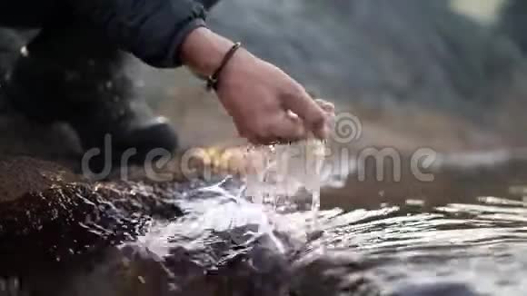 一个徒步旅行者把手伸进一条冰冷的河里视频的预览图