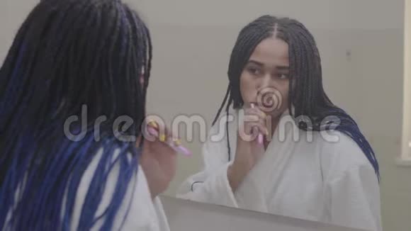 镜子里的非裔美国妇女刷牙年轻人早上在浴室里准备美容视频的预览图