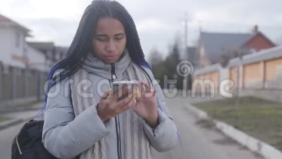 美丽的非洲裔美国女孩与可怕的站在街上和使用智能手机聪明的青少年利用社交视频的预览图