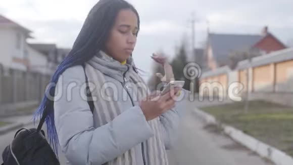 年轻漂亮的非裔美国女人站在街上拿着智能手机环顾四周迷失少年视频的预览图