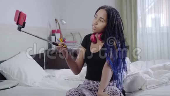 镜头接近可爱的非裔美国女孩拿着自拍棒与智能手机和交谈青少年视频的预览图