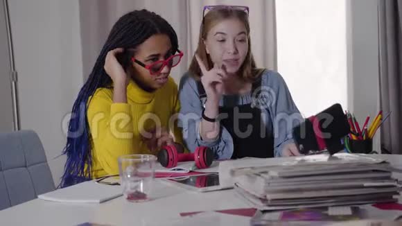 白种人金发女孩和她的非洲裔美国朋友扎着辫子在智能手机的自拍相机上交谈视频的预览图