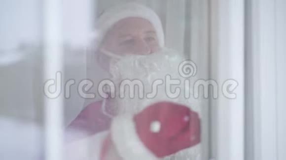 老人穿着圣诞老人服装打开窗户打电话给他的朋友听他回答然后挥手视频的预览图