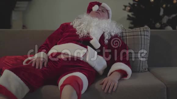 醉汉假白胡子穿着圣诞老人的服装躺在家里的沙发上挥舞着手坏圣诞老人视频的预览图