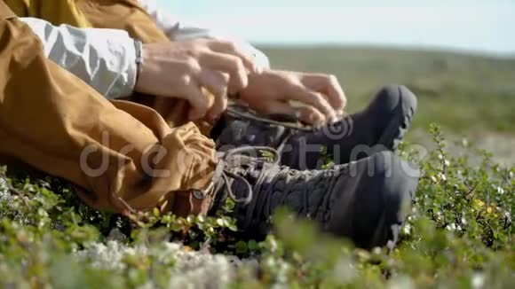 一个徒步旅行者把鞋子系在冻土带的草地上视频的预览图