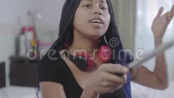 非裔美国人少女看智能手机屏幕和显示新耳机的肖像年轻女子录音视频的预览图