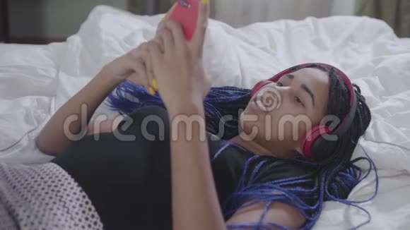 非裔美国少女戴着可怕的屁股在智能手机上打字在耳机里听音乐时动动脑袋视频的预览图