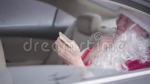 老圣诞老人坐在车后座上摘下假胡子舔着手指数着一包美元视频的预览图
