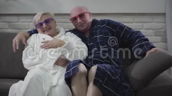 积极的老白种人夫妇坐在沙发上看3D电影的特写年长的丈夫和妻子视频的预览图