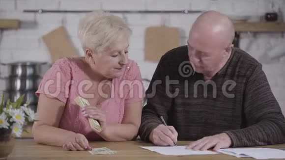 高加索族夫妻的特写以解决他们的财务问题女人拿着现金男人写下来老配偶视频的预览图
