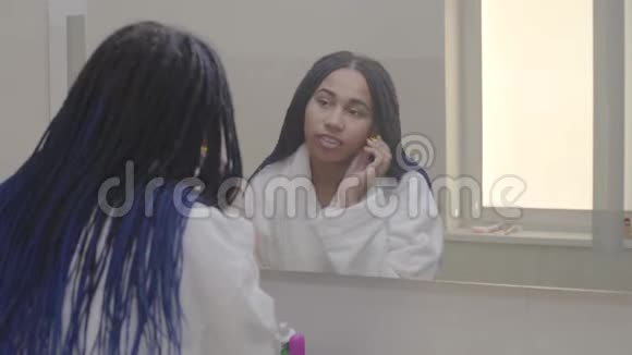 十几岁的非裔美国女孩欣赏她在大镜子里的倒影的肖像可爱的青少年在浴室里度过早晨视频的预览图
