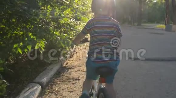 在公园日落或日出时骑自行车的带蓝色头盔的小男孩视频的预览图