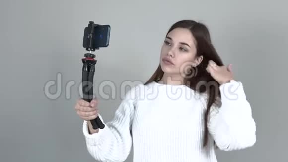 一位白人女孩博主拿着一个三脚架手里拿着一部电话她的头发变得笔直视频的预览图
