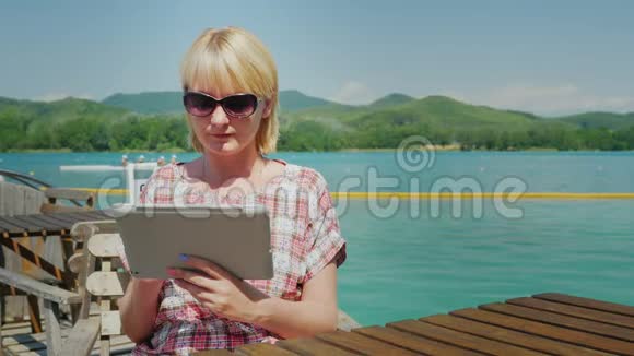 带着药片的年轻女人坐在露台上的咖啡馆里背景是风景如画的湖泊和绿色视频的预览图