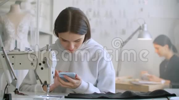 女裁缝看着工作场所的智能手机屏幕给顾客写短信视频的预览图