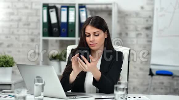 自信的商业女性打字号码用智能手机打电话看手提电脑屏幕视频的预览图