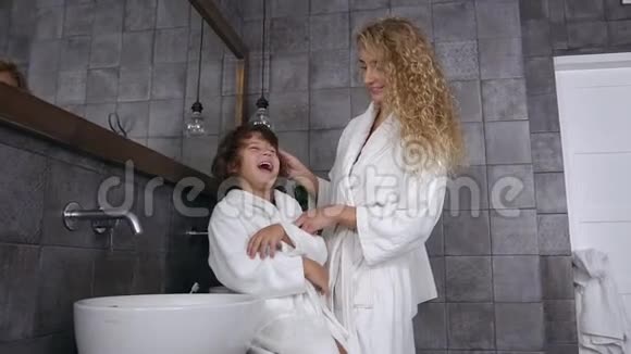 可爱的金发女郎穿着晨衣在浴室里梳着刷子的卷发视频的预览图
