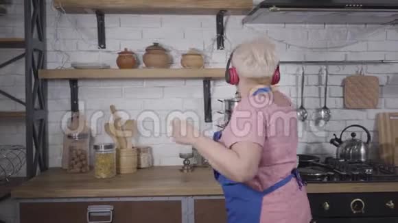 后景特写积极的高级白种人妇女在厨房做饭时跳舞成熟的活力舞蹈视频的预览图