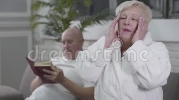 悲伤的白种人女人的肖像头痛坐在白色的浴袍和摩擦寺庙她丈夫坐在视频的预览图