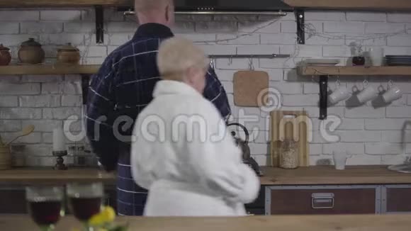 在厨房做饭的成熟白种人夫妇资深妻子和丈夫在浴袍上共度时光视频的预览图
