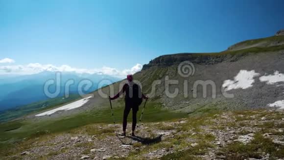 女人在美丽的高加索山脉徒步旅行在去山顶的路上带着背包和徒步旅行杆的年轻女子视频的预览图