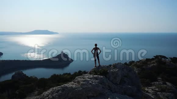 女徒步旅行者在山上的海洋享受美丽的景色和周围的野生自然在日出胜利和成功视频的预览图