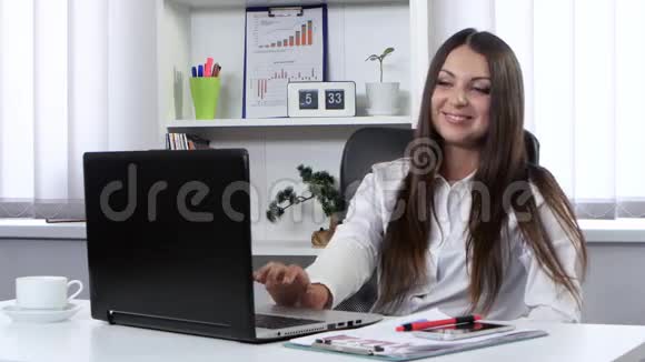 商务女性坐在办公室手提电脑前在网络摄像头上交谈她开心而微笑视频的预览图
