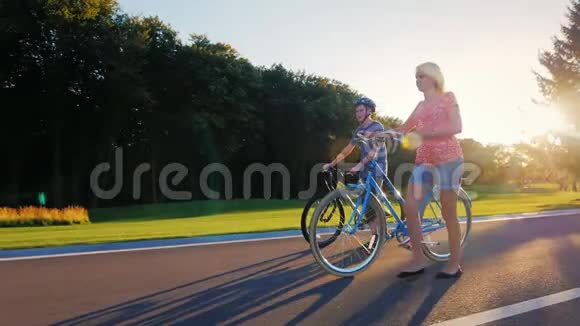 steadicam射击妇女和儿子骑自行车在公园里行走日落时分视频的预览图