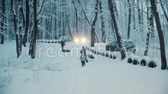 孩子们在下雪的冬天森林里玩充气戒指停在附近的汽车视频的预览图