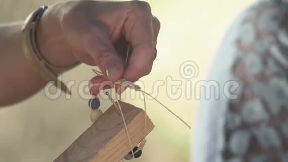 一个女人的双手用珠子绑着一根绳子做一个珠宝手镯视频的预览图