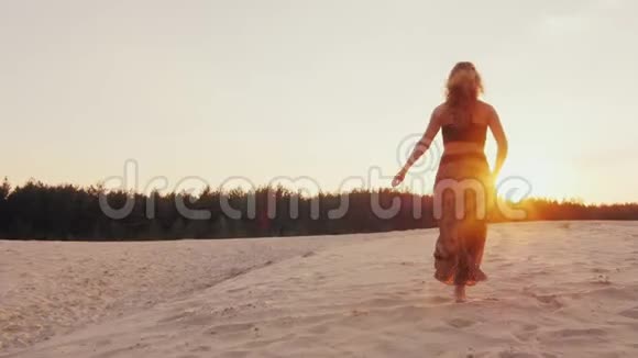 年轻的女人穿着一件漂亮的衣服光沿着海滩跑进日落把他的手臂伸向太阳概念视频的预览图