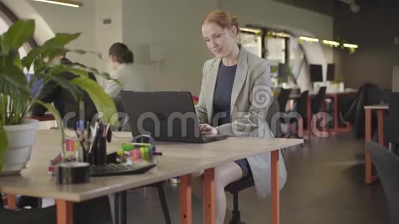自信的白人红头发女人在办公室用笔记本电脑工作的肖像文雅的年轻女上班族视频的预览图