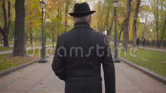 一位白发白种人的背影他戴着优雅的黑色帽子穿着外套在巷子里漫步成熟的男人视频的预览图