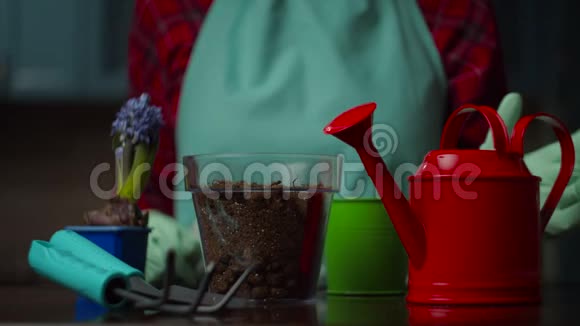 女性手在手套中缓慢地在透明花盆中拿红色的浇水罐和浇水地面国内视频的预览图