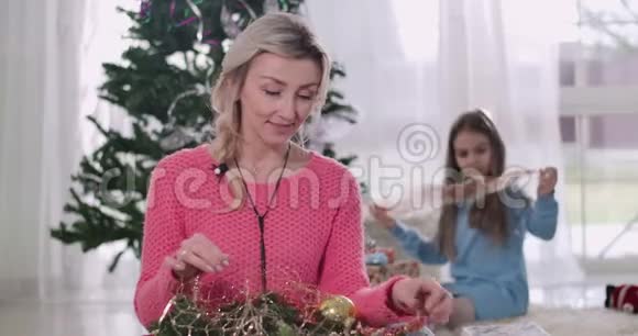 布鲁内特高加索女孩选择圣诞装饰的背景她的母亲坐在前台和视频的预览图