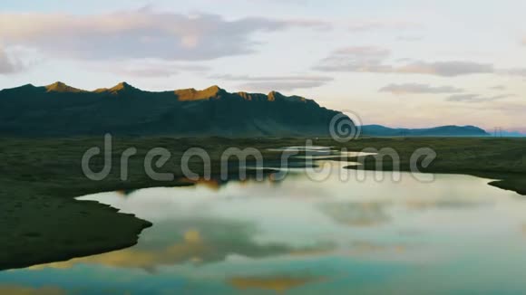 无人机飞过水面美丽的山形倒影进入靠近火山土地的小湖冰岛的汽车在高速公路上行驶视频的预览图