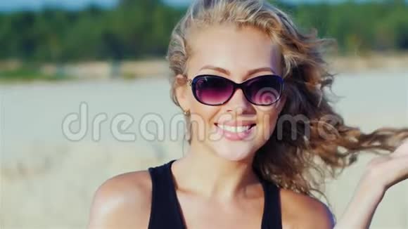 一个年轻迷人的女人微笑着看着镜头在海滩上摆姿势的肖像视频的预览图