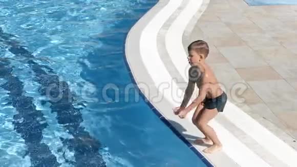 活跃的晒黑男孩在游泳池里跳跃周围是飞溅的水慢动作视频的预览图