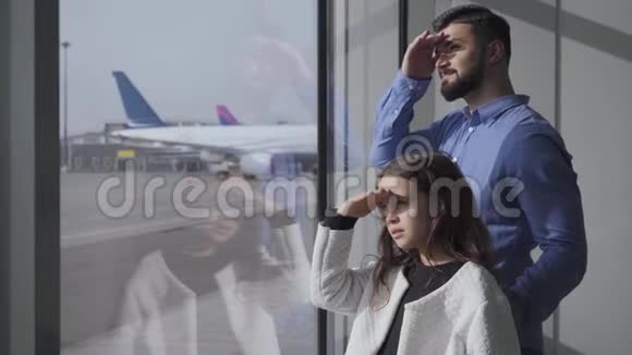 侧面观察特写白人男子和小女孩看着玻璃机场窗口在跑道父亲和视频的预览图