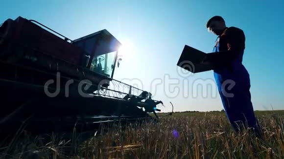 农民在田里检查拖拉机用笔记本电脑工作农民在农田上视频的预览图