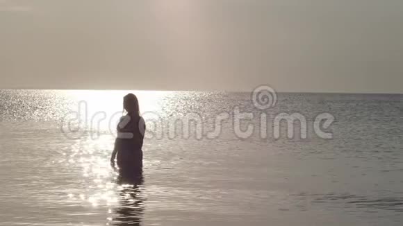 黎明时分一位身穿泳装的美女站在平静的大海中间太阳光线和眩光作用在水面上视频的预览图