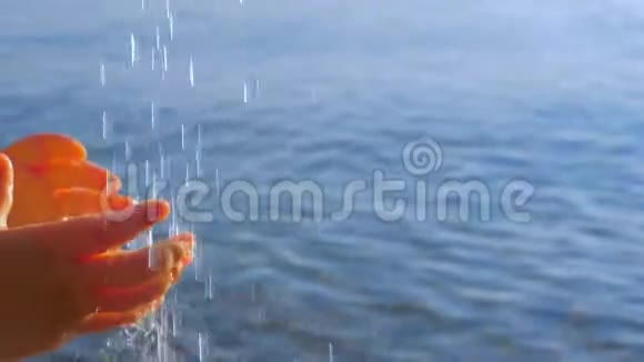 孩子们伸手去拿水滴水从顶部倾泻到海景背景上的小孩手上视频的预览图