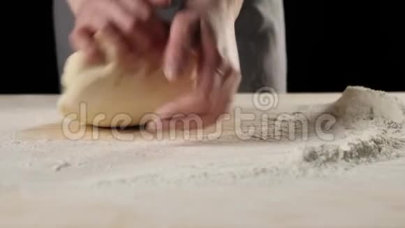 专业的面包师把面团揉在靠近面粉堆的木桌上背景是黑色的烹饪比萨饼的概念视频的预览图