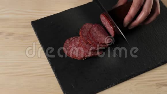 专业厨师用锋利的金属刀在黑色背景下的黑板上切割腊肠面团揉捏的概念视频的预览图