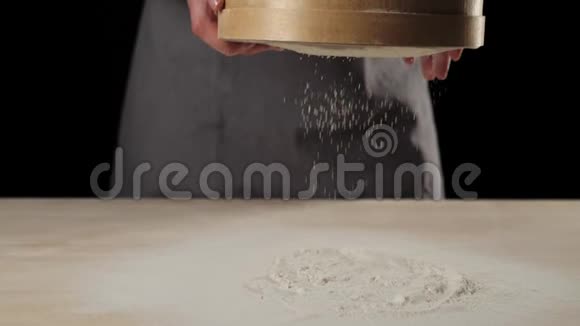 专业的面包师用黑色背景的木筛筛面粉掉落的白色颗粒视频的预览图