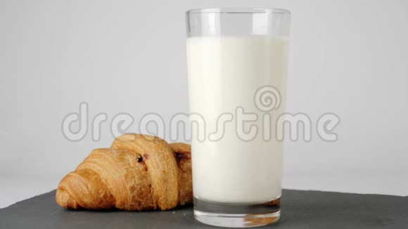 新鲜的白牛奶放入透明的玻璃中靠近牛角面包巧克力在白色桌子上的黑板上旋转视频的预览图