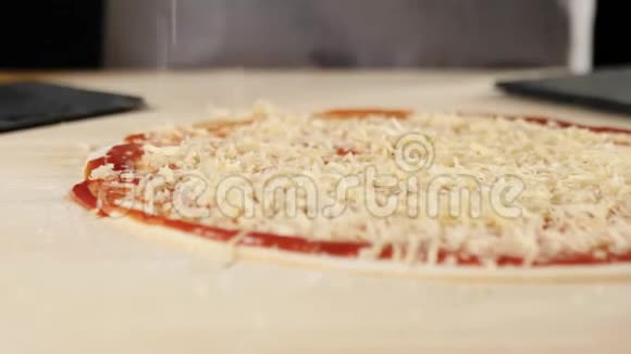 专业厨师将磨碎的奶酪倒入一个披萨基地桌子上放着番茄酱上面装饰着披萨配料视频的预览图